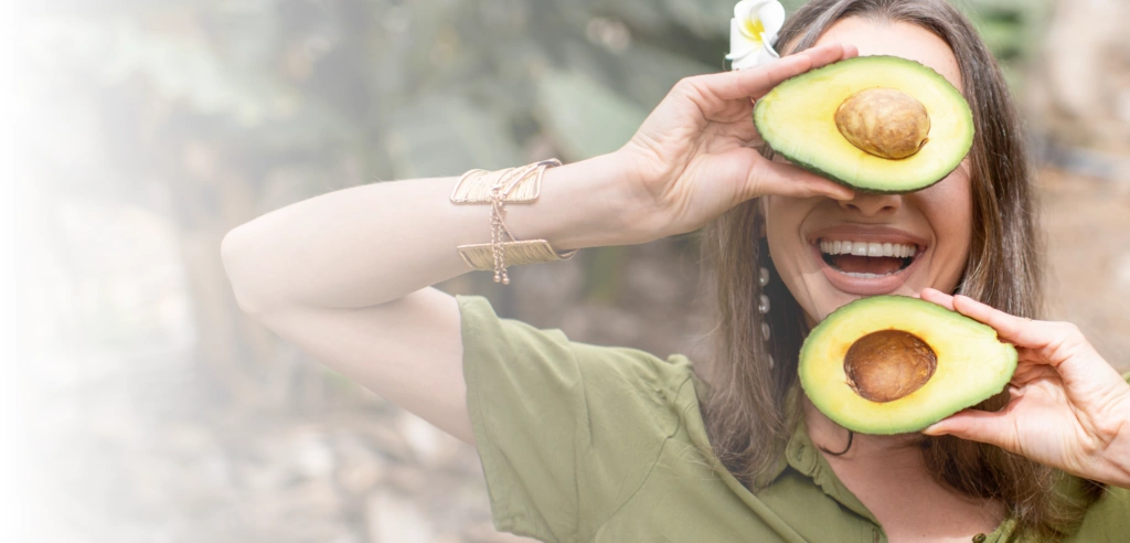 Ernährung für die Haut: Frau hält Avocado vors Gesicht
