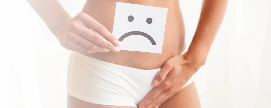 Person hält Schild mit traurigem Smiley vor den Schritt