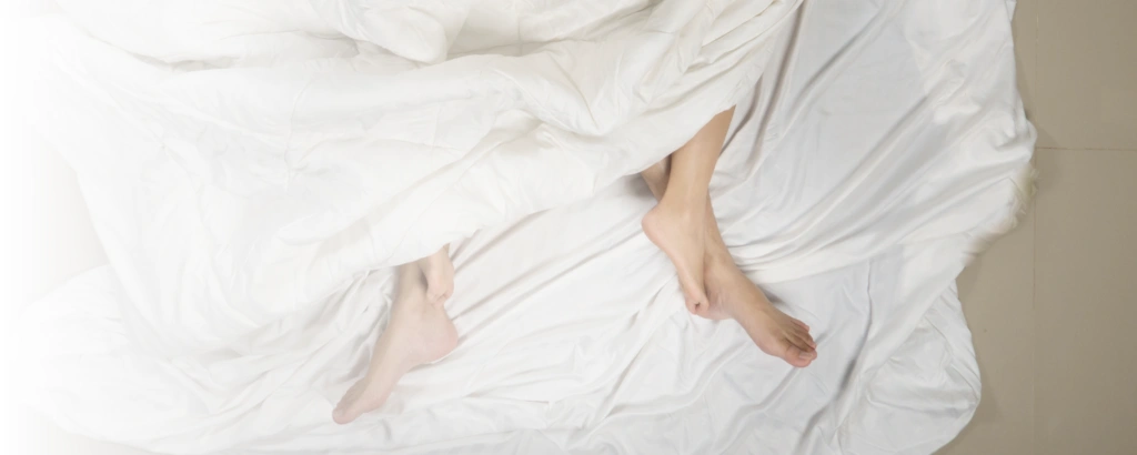 Zwei Personen liegen im Bett und man sieht die Füße